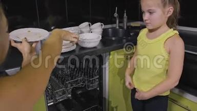 妈妈教女儿聪明的女孩学习使用洗碗机。 年轻的女主人孩子们在装<strong>脏盘子</strong>